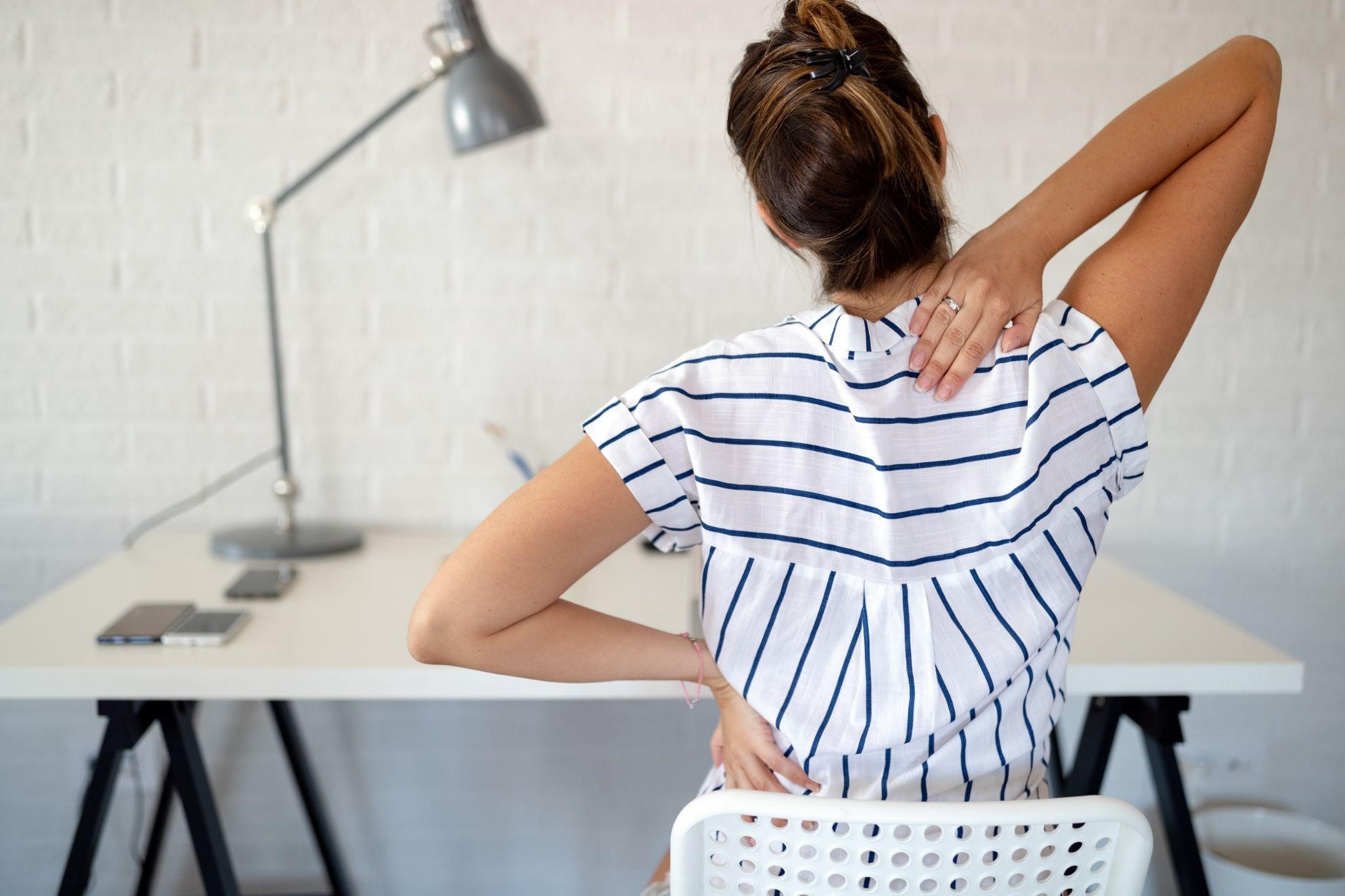 Woman holding her back while sitting at a desk
